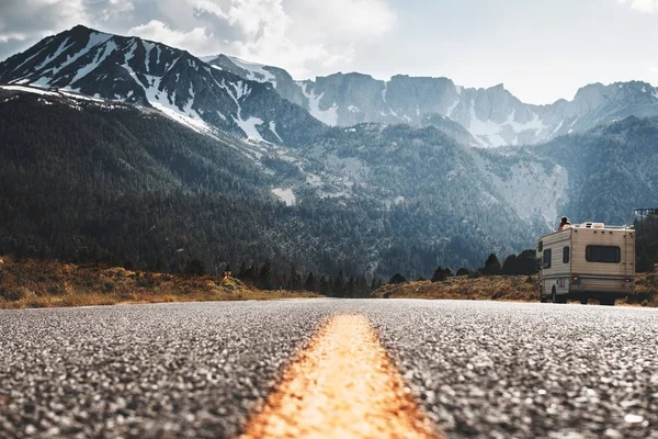 RV camper stands on side of road on background of huge mountain. Friends travel to motorhome on mountain road. Travelers rest on sidelines and enjoy mountain view — Stock Photo, Image