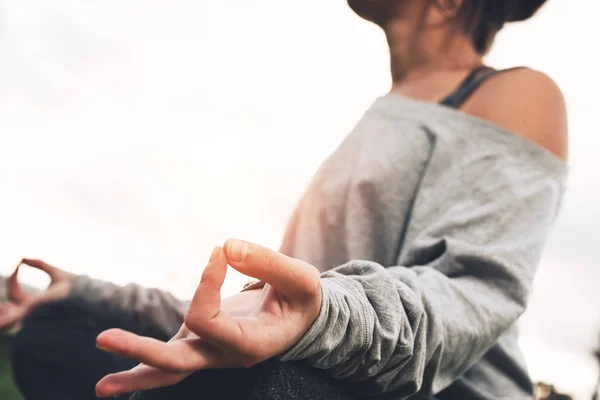 Detailní pohled na ženy ruce v meditační pozici. Nádherná dívka dělá jógu v městském parku na trávníku po náročném dni při západu slunce. Vertikální, rozmazané pozadí, sluneční světlo a světlice — Stock fotografie