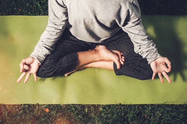 Retrato de una joven esbelta practicando yoga en pose de loto sobre césped verde. Hermosa chica haciendo asana relajante en parque urbano. Vista superior. Concepto relax y calma —  Fotos de Stock