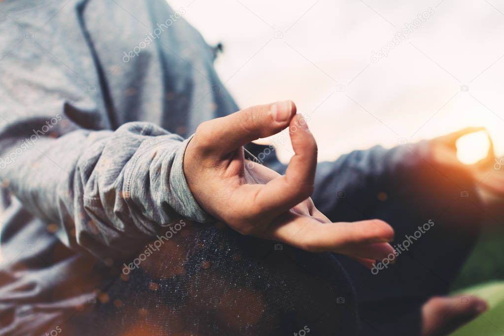 Close up view of female hands in meditation pose. Young girl practicing yoga in urban environment at sunset after a hard day. Concept of relaxation and rest in city park. Blurred background, flares