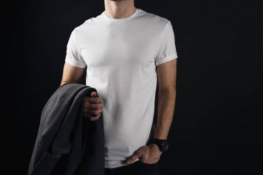 Atletik genç adam beyaz boş tshirt giyer ve bir kat elinde tutuyor. Siyah bir arka plan üzerinde beyaz bir t-shirt hipster duruyor