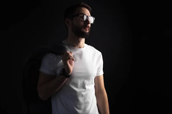 Skäggig ung hipster i glasögon poserar med kappa i vit blank t-shirt på svart bakgrund — Stockfoto