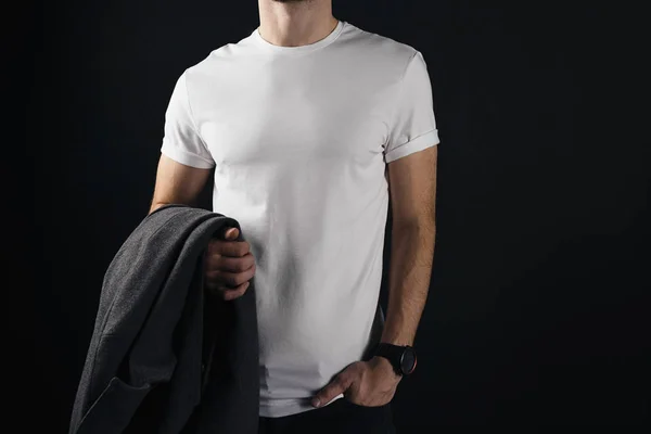 Athletic young man wears white blank tshirt and holds a coat in his hand. Hipster stands in a white t-shirt on a black background