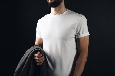 Spor erkek vücut yakın çekim siyah arka plan üzerinde beyaz boş t-shirt giyiyor. Boş tshirt poz ve bir kat elinde tutan sakallı hiptser