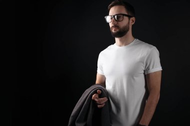 Güzel sakallı hippi gözlük ve boş beyaz tshirt giymiş ve elinde siyah bir zemin üzerine bir kat tutar