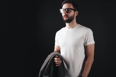 Genç dalgın iş adamı boş beyaz t-shirt giyen gözlük sakallı ve ceket siyah arka plan üzerine tutar