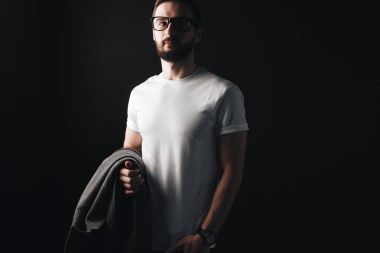 Boş beyaz t-shirt üzerine siyah bir arka plan üzerinde duran genç sakallı işadamı. Yenilikçi bir ceket ve gözlük bir beyaz tshirt poz ile