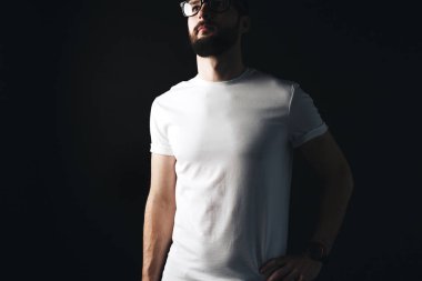 Genç işadamı koyu arka plan üzerinde boş beyaz tshirt sakallı. Hipster boş t-shirt ve gözlük