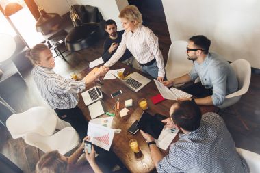 Coworking gençlerin grup karşılamak ve bir anlaşma. Erkek ve kadın iş ortakları arasında karşılıklı olun. Yaratıcı yöneticileri oturup dizüstü bilgisayarlar ve kağıt belgeleri içeren tablo
