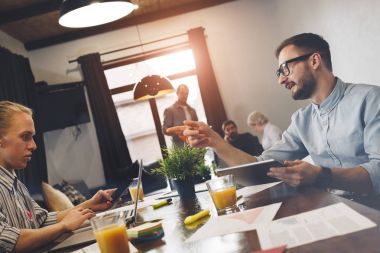 Modern odaya birlikte çalışan takım coworking. İki adam masa etrafında oturup modern dizüstü ve tablet üzerinde çalışmak. Yeni bir başlangıç tartışma