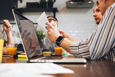 İşadamı ile bir smartwatch elinde bir kağıt belgeyi düzenliyor. Grup arkadaşları masa etrafında oturur. Takım çalışması ve beyin fırtınası kavramı