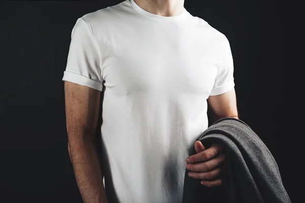Mężczyzna sportowe i smukłe ciało sobie w biały tshirt puste i przytrzymując płaszcz w ręku na ciemnym tle — Zdjęcie stockowe