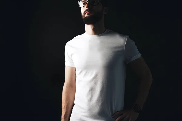 Młody Brodaty biznesmen w pusty biały tshirt na ciemnym tle. Hipster sobie pustej t-shirt i okulary — Zdjęcie stockowe