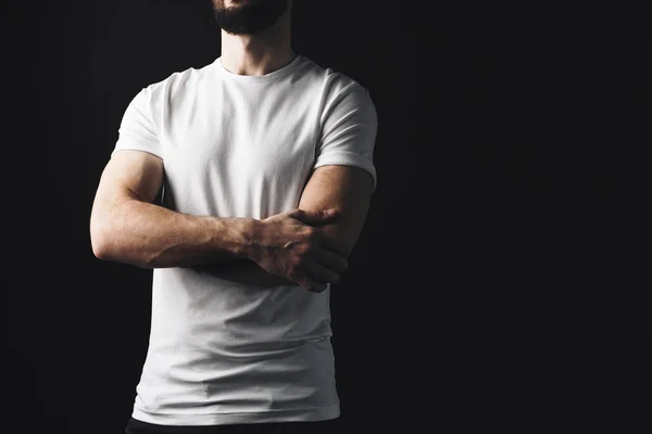 Homem musculoso cruzando os braços no peito vestindo t-shirt branca. Desportivo cara cruzando as mãos posando em tshirt vazia no fundo escuro — Fotografia de Stock