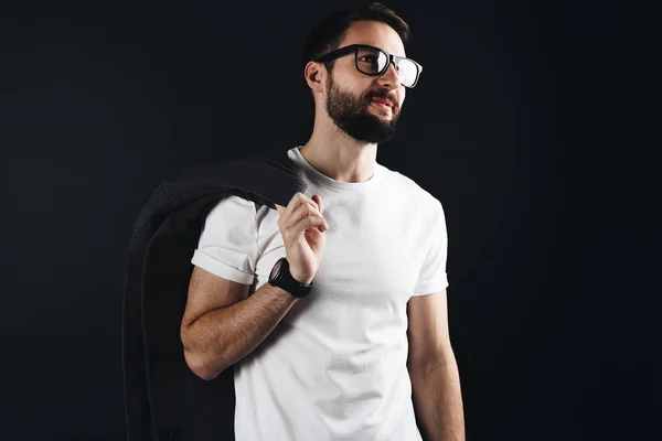 Hombre barbudo feliz en gafas con abrigo en el hombro con camiseta blanca en blanco sobre fondo negro — Foto de Stock