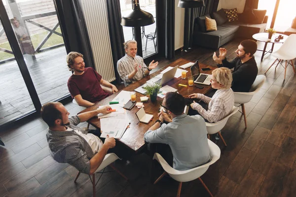 Reunión de coworking. Los empresarios del grupo se sientan alrededor de la mesa y trabajan en computadoras portátiles y tabletas. Equipo de inicio discutiendo nuevo proyecto juntos — Foto de Stock