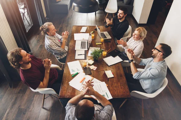 Grupo de gerentes creativos trabajan juntos moderno estudio de coworking. Jóvenes conversando con sus socios.Equipo de inicio. Reunión alrededor de mesa de madera — Foto de Stock