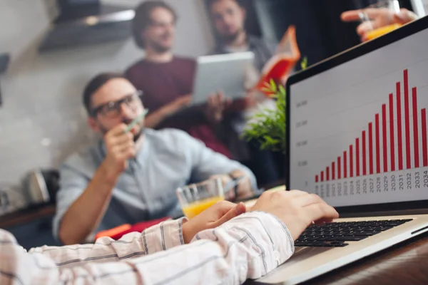 Group of young coworkers or finance analysts discuss about company indicators. Graph and diagram on laptop screen. Teamwork process concept — Stock Photo, Image