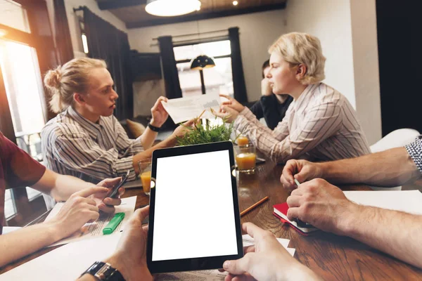 POV näkymä valkoinen tyhjä näyttö tabletti miesten käsissä ja ryhmä nuoria coworking ihmiset keskustelevat uuden hankkeen käynnistymistä avoimessa tilassa. Tiimityö — kuvapankkivalokuva