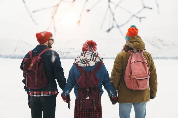 Группа из трех друзей стоят, держась за руки и наслаждаясь снежными горными вершинами. Компания хипстеров стоит перед удивительным видом на зиму. Носит рюкзак. Стиль жизни — стоковое фото