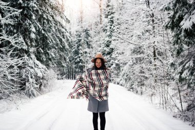 Güzel kız rahat kareli atkı ve şapka giyen karlı ağaçları arasında kış ormanda yürüyüş. Boho stili