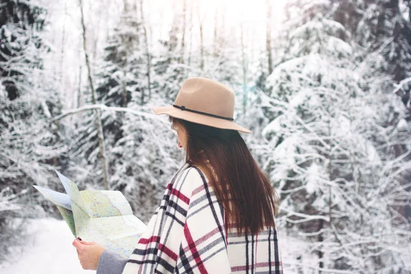 Handsome woman wearing plaid scarf and hat traveling in snow forest and hold map in hand