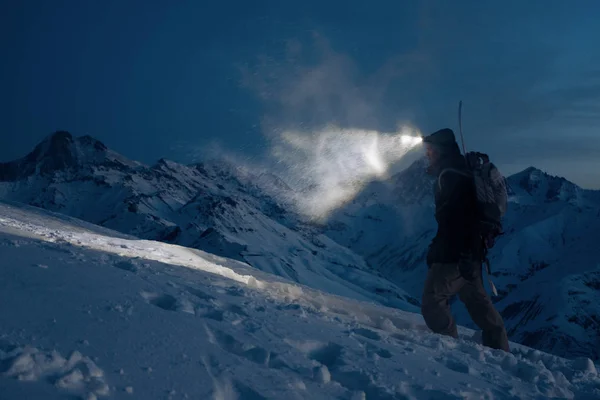 Profesyonel expeditor tamamlama yolu bir Far ile gece ve ışıklar karlı dağlara tırmanmak. Kayak Giyim, sırt çantası ve arkasından bir snowboard üzerinde. Backcountry ve tur kayağı