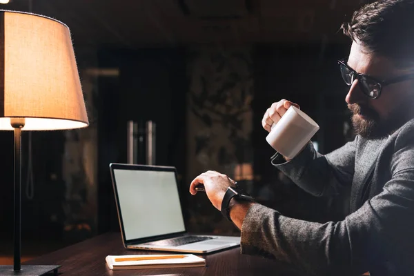 Joven Hombre Negocios Barbudo Sostiene Una Taza Mira Smartwatch Mano — Foto de Stock