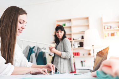 Genç kadın dressmaster dikiş showroom çağdaş dizüstü bilgisayar ile yeni konsept giyim oluşturun. Küçük işletme. Terzi kumaş atölye ile çalışma
