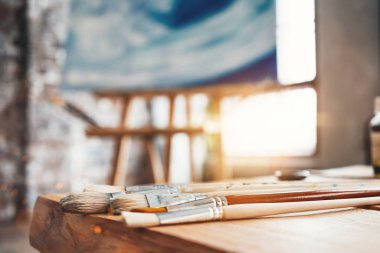 Sanatçı yakın çekim stüdyo ahşap bir masa üzerinde Boya fırçaları. Arka plan tuval şövale üzerinde. Ressam atölyesi. Etkisi flare. Yaratıcı kavramı