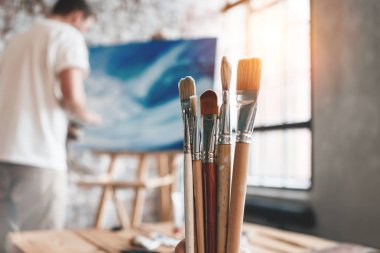 Tuval veya çizimin arkasına atölyesinde çalışan adam ressam. Fırçalar Studio ahşap masa üzerine kapatın. Etkisi flare. Loft classe sanatçı