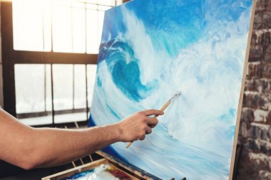 Sanatçının tuval şövale üzerinde arka plan üzerinde boya fırçası tutan erkek el. Loft Studio dalga okyanus çizim profesyonel ressam. Hobi kavramı