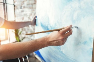 Sanatçı portre tuval şövale üzerinde arka plan üzerinde boya fırçası tutan erkek eli. Loft Studio dalga okyanus çizim ressam. Etkisi flare. Hobi kavramı