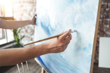 Sanatçı portre tuval şövale üzerinde arka plan üzerinde boya fırçası tutan erkek eli. Loft Studio dalga okyanus çizim ressam. Etkisi flare. Hobi kavramı