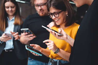 Yetişkin bir grup mutlu hipster sırada bekliyor ve modern akıllı telefonları kullanıyorlar. Pozitif iş ekibi dijital telefonu beklemede tutun.