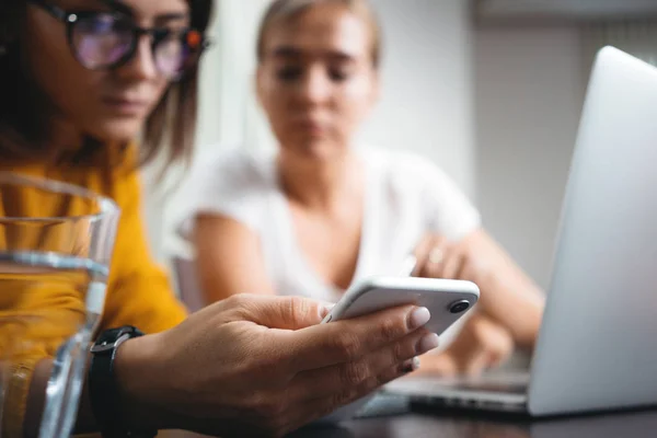 Group of happy woman working together and using digital gadgets at open space. Close-up of female hands hold modern smartphone at her workplace at office