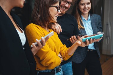 Yetişkin bir grup mutlu hipster sırada bekliyor ve modern akıllı telefonları kullanıyorlar. Pozitif iş ekibi dijital telefonu beklemede tutun.