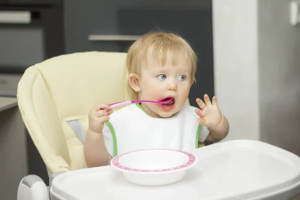 Küçük bir çocuk tabaktan kaşıkla yer, sandalyeye oturur.