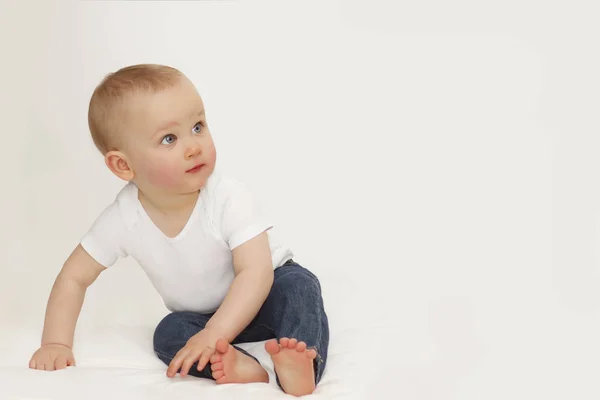 Portret van een kind met blauwe ogen op een grijze achtergrond In jeans en een witte T-shirt — Stockfoto