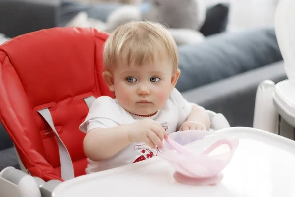 Ребенок с голубыми глазами блондинка сидит и ест кашу — стоковое фото