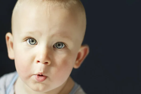 Een jonge, ernstige baby is staren naar de camera geïsoleerd op een zwarte achtergrond. De childs ogen zijn blauw. — Stockfoto