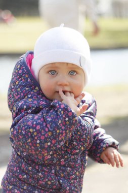 Mavi gözlü küçük bir kız sokak portresi. Bir kız bir arka plan taşlar ve otlar üzerinde duruyor.