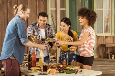 multiethnic friends clinking with glasses at picnic clipart
