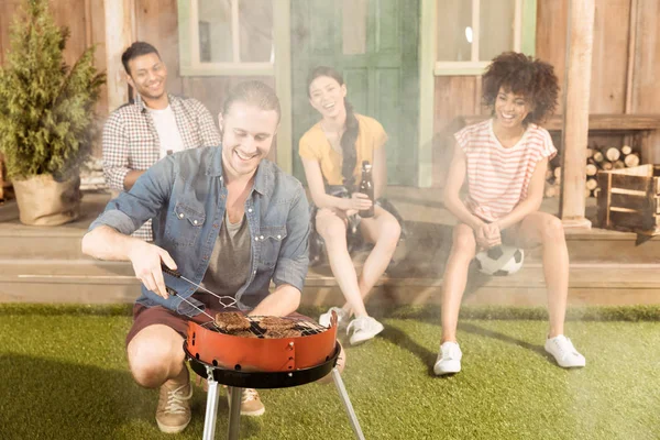 Man preparing barbecue while friends sitting — Stock Photo, Image