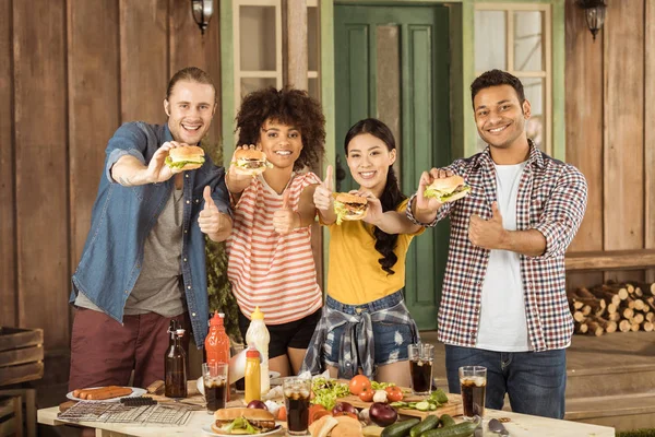 Friends holding burgers and showing thumbs up — Stock Photo, Image