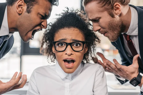 Hombres de negocios gritando a la mujer de negocios en la oficina - foto de stock