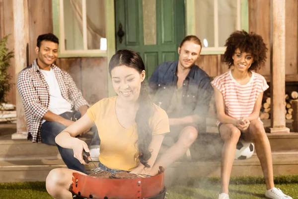 Donna preparare barbecue mentre gli amici seduti — Foto stock