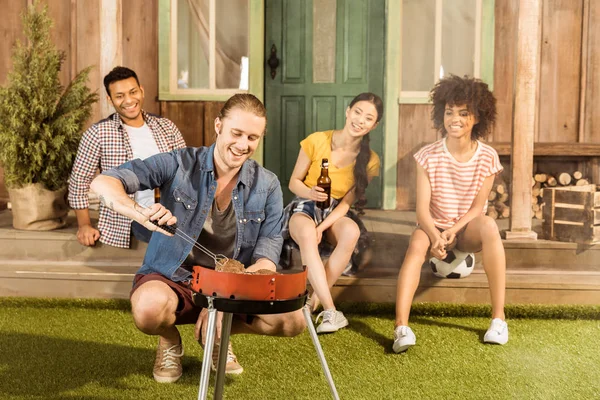 Uomo preparare barbecue mentre gli amici seduti — Foto stock