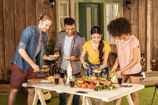 Multiethnic friends making burgers at picnic — Stock Photo