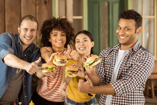 Sonrientes amigos multiétnicos sosteniendo hamburguesas - foto de stock